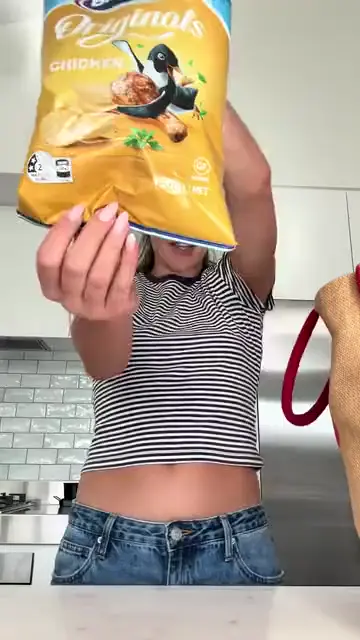 A woman leaning on her kitchen bench holding up a bag of chicken chips