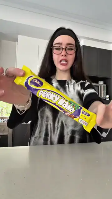 A woman in glasses holding up a chocolate bar to show the camera