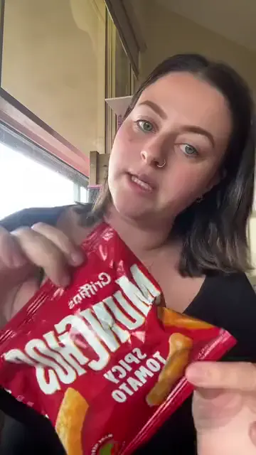 A woman opening a bag of spicy tomato snacks