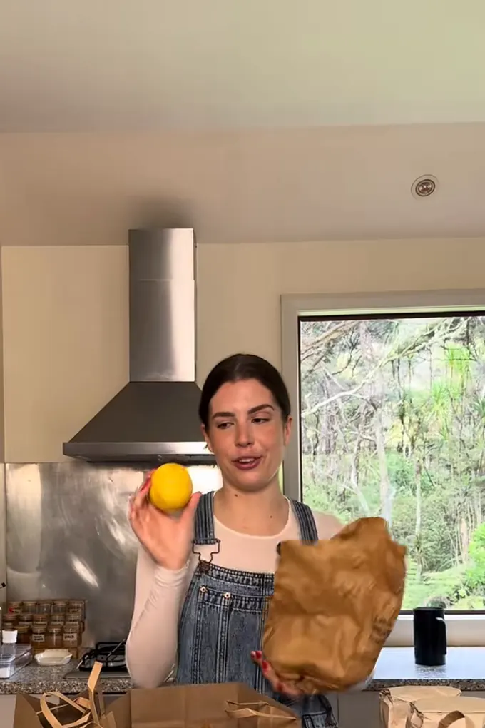 Example post, a reel: a woman in her kitchen unpacking grocery bags and holding up a lemon